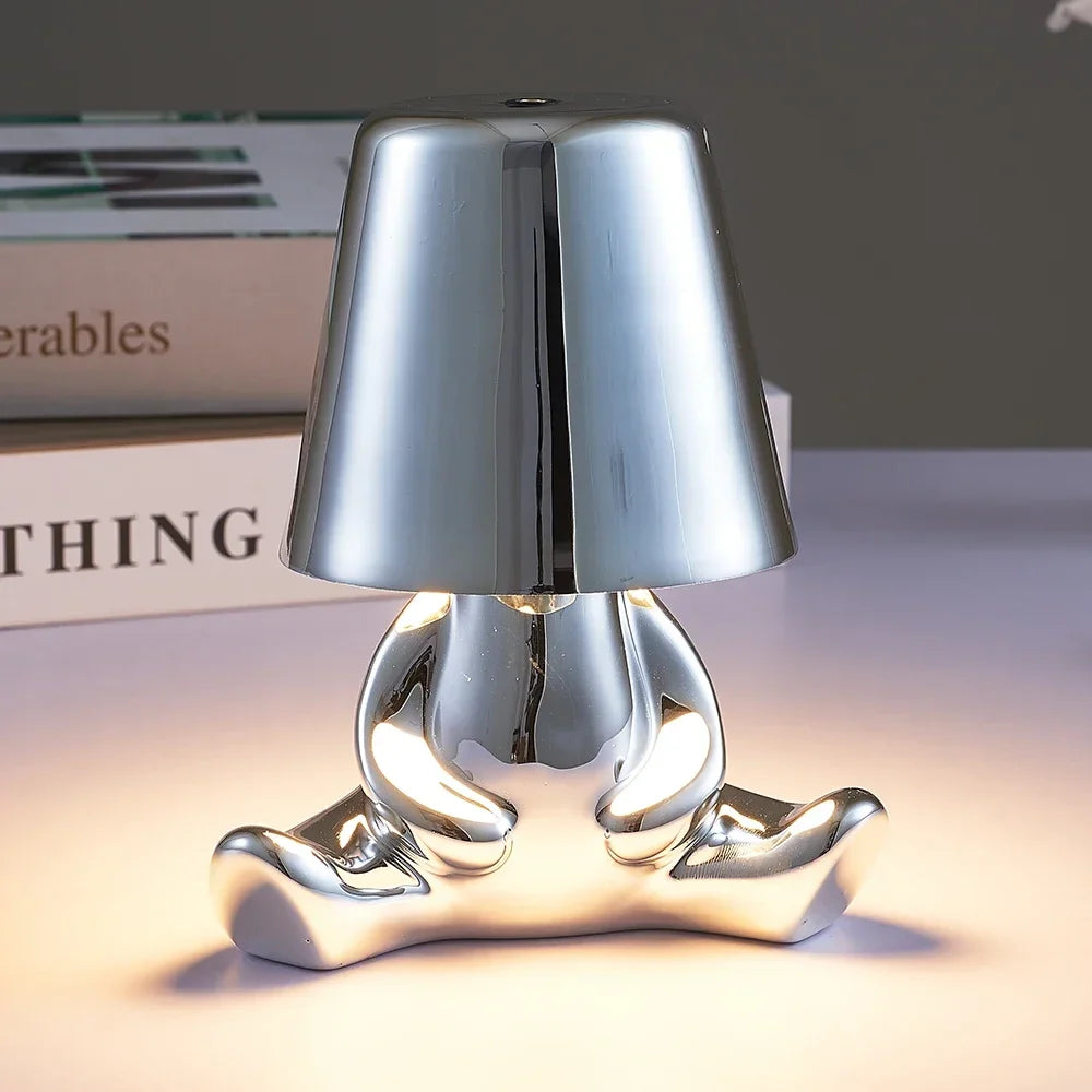 Designerska lampa stołowa LED — figurka w pozycji siedzącej, połyskujące wykończenie | Norivo Norivo