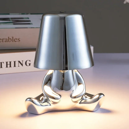 Designerska lampa stołowa LED — figurka w pozycji siedzącej, połyskujące wykończenie | Norivo Norivo